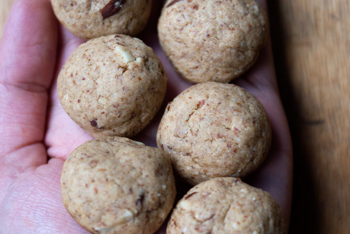 Close-up picture of six small round almond cookies (bitterkoekjes in Dutch) sitting on the palm of a hand resting on a wooden table.