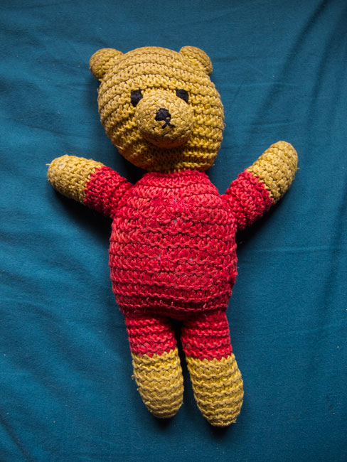 Picture of a yellow and red cotton knit teddy bear on a turquoise background.