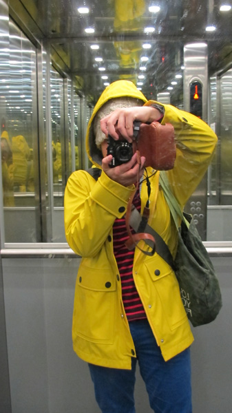 Mirror selfie of a person in a bright yellow raincoat, blue pants and red striped sweater.