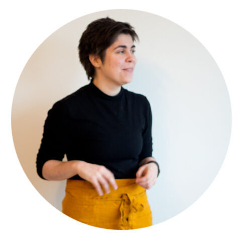 Picture of aster wearing a black turtleneck and a bright yellow apron.